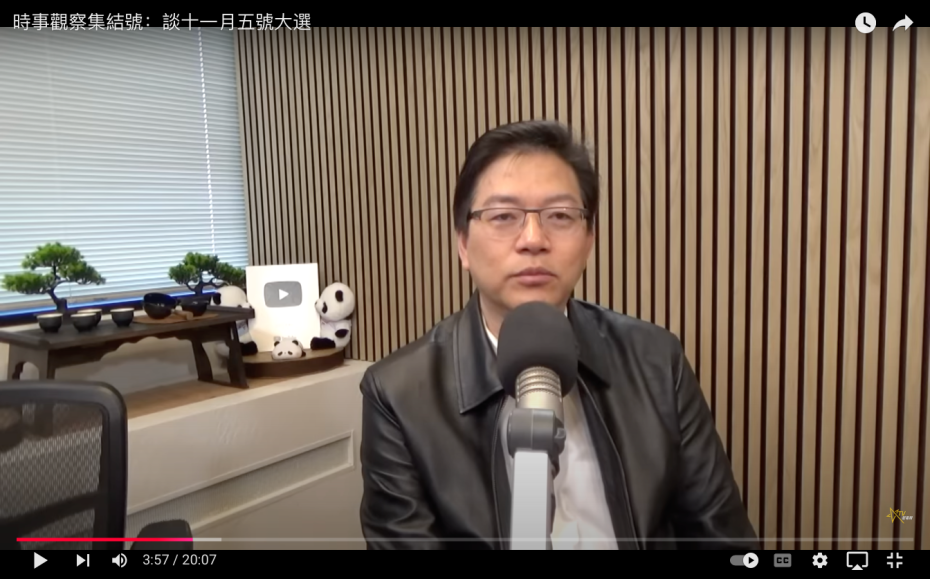 A man in a leather jacket sits in front of a microphone in a studio with wood paneling and shelves holding decorations, including a YouTube play button.